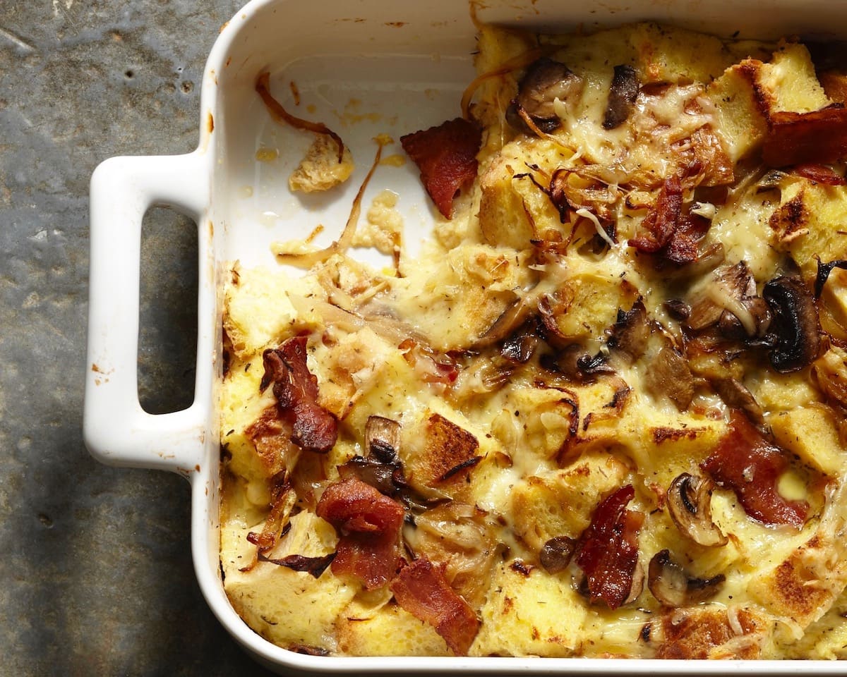 Onion Bacon Mushroom bread pudding in white casserole dish with a serving missing