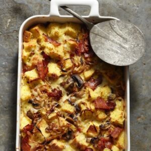 Onion Bacon Mushroom Starta in white casserole dish with metal serving spoon