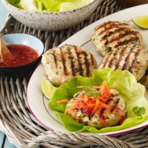 Thai Turkey Burger patties on white plate with lettuce sauce and shredded carrots