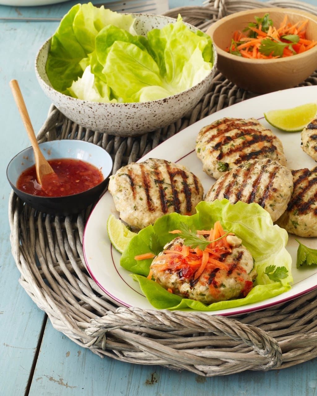 Thai Turkey Burger patties on white plate with lettuce sauce and shredded carrots