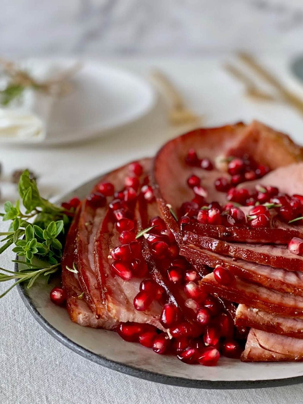 close up of cooked ham slices on platter with pomegranate and herbs