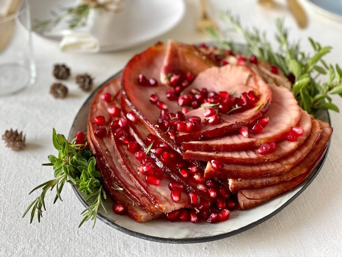 spiral cut ham with pomegranate arils on platter with herbs