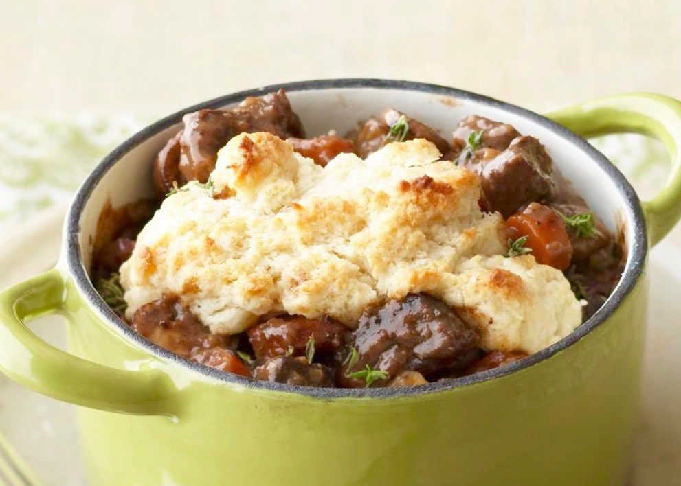 beef and vegetables stew with biscuit topping in green pan