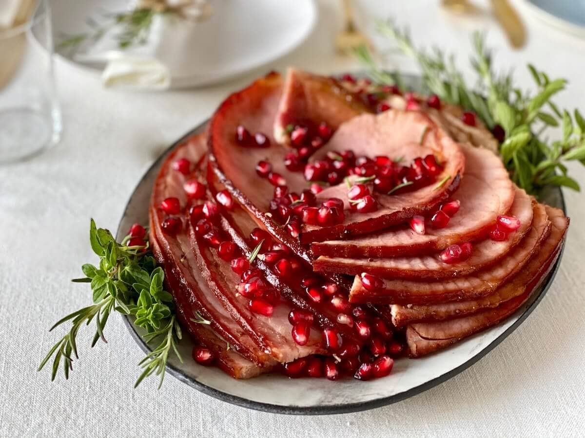 sliced holiday ham on platter with pomegranates