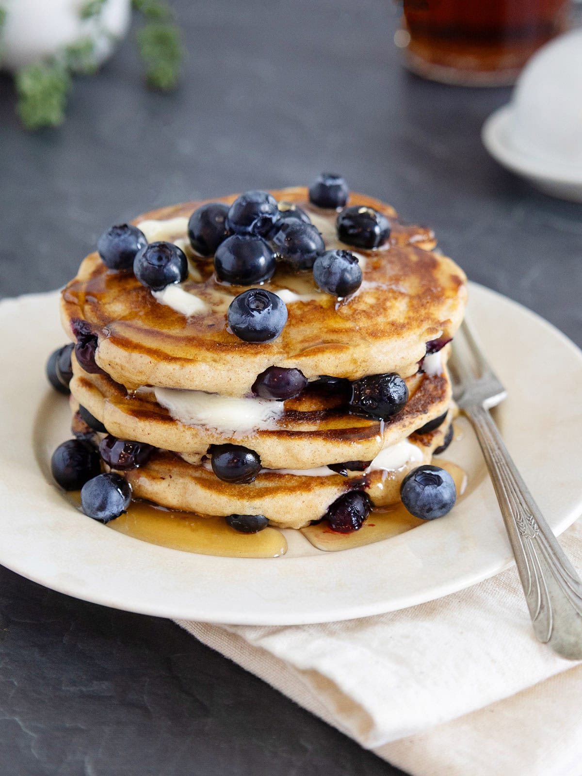 A stack of blueberry pancakes topped with butter, syrup and fresh berries.