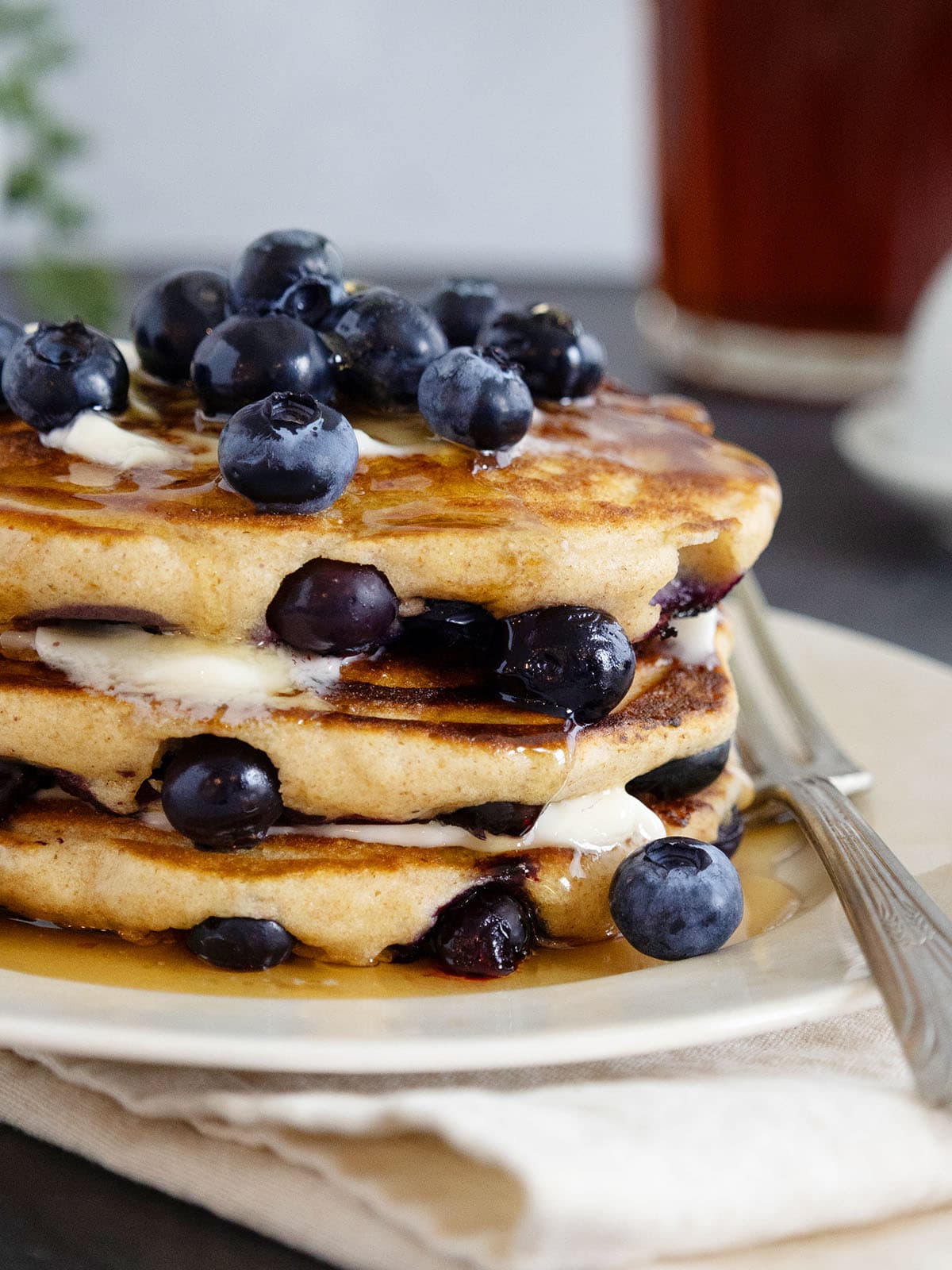 Close up of the side of a stack of blueberry pancakes topped with butter, syrup and fresh berries.