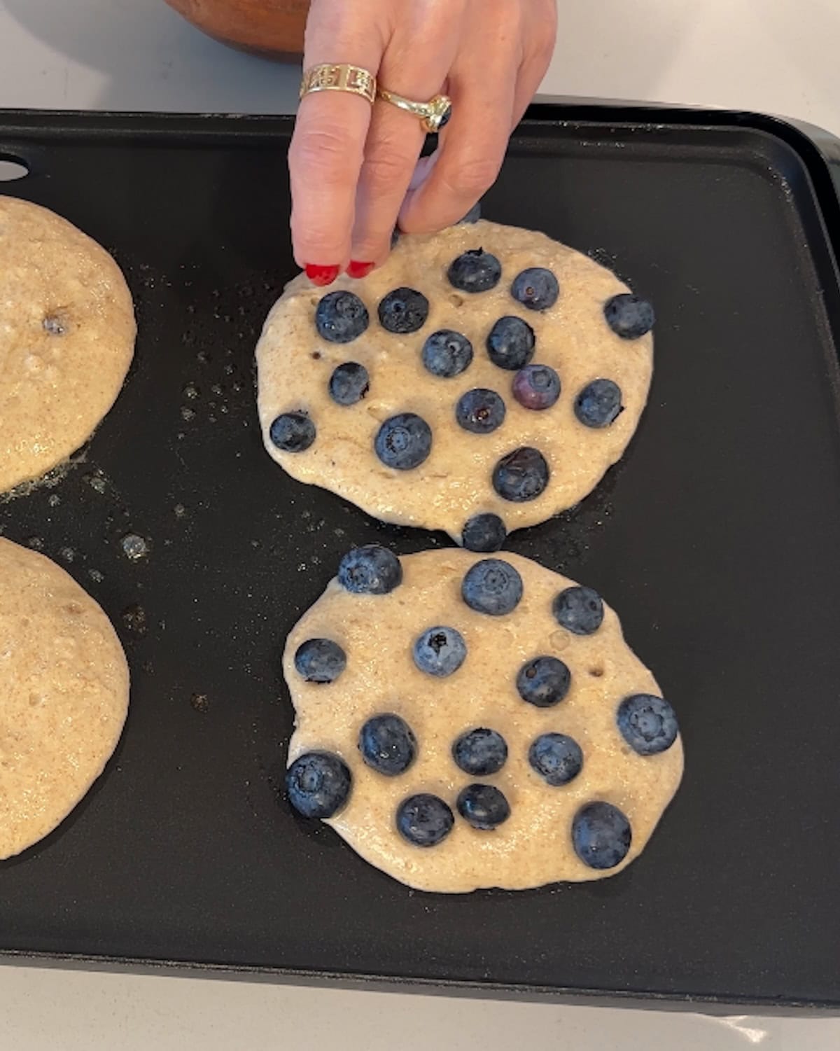 Placing blueberries on top of cooking pancakes.