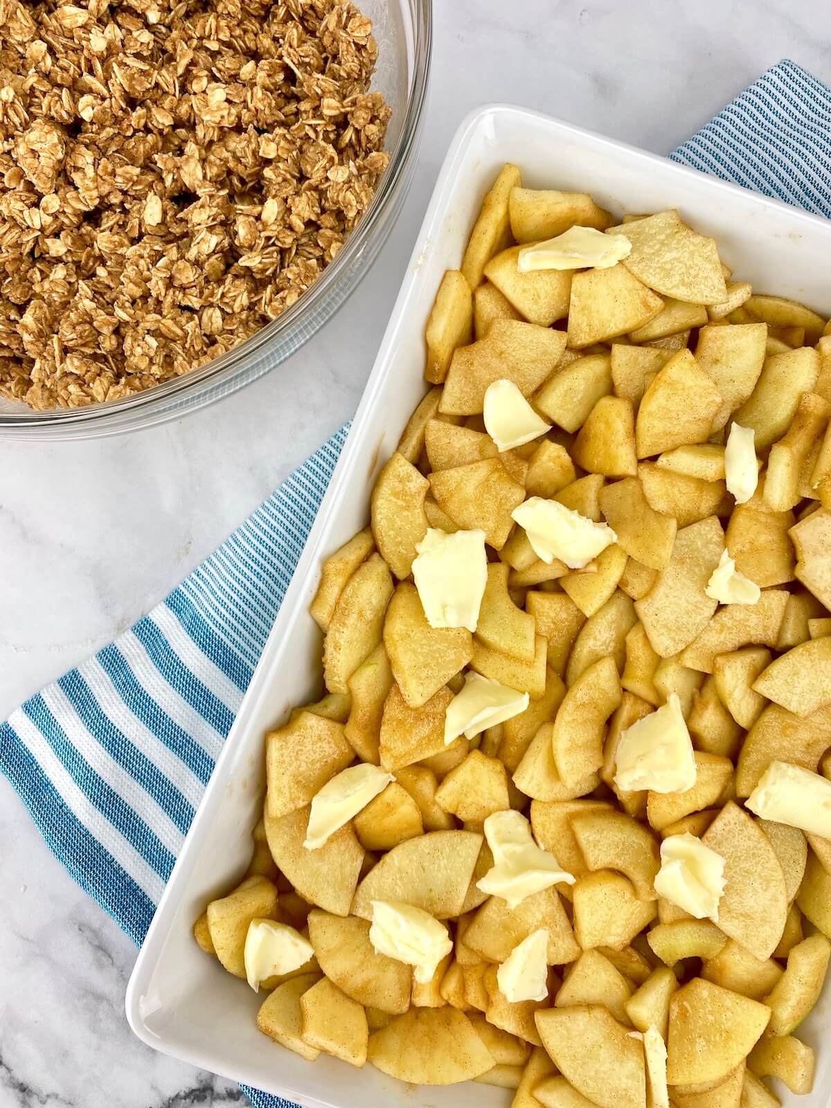 apples and butter in white 9 by 13 dish with oat topping to the side