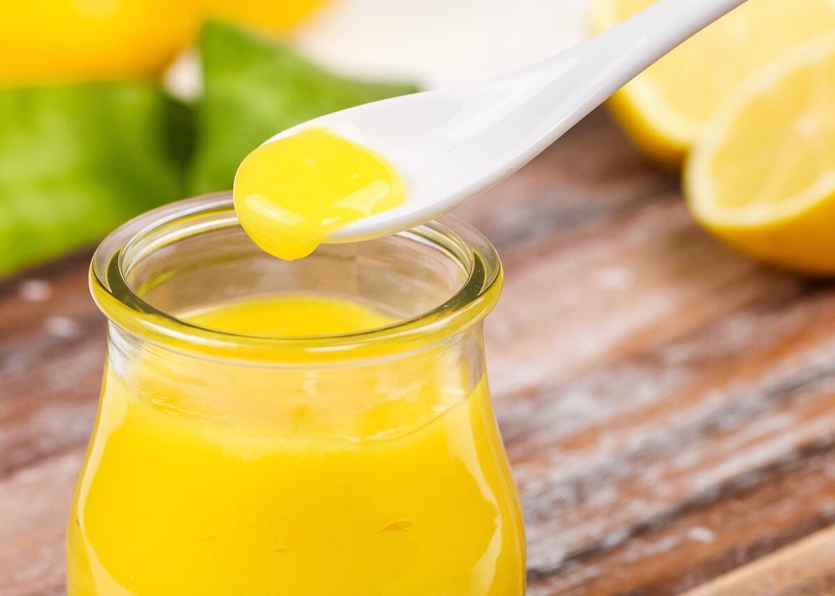 spooning lemon curd from a jar on a white spoon