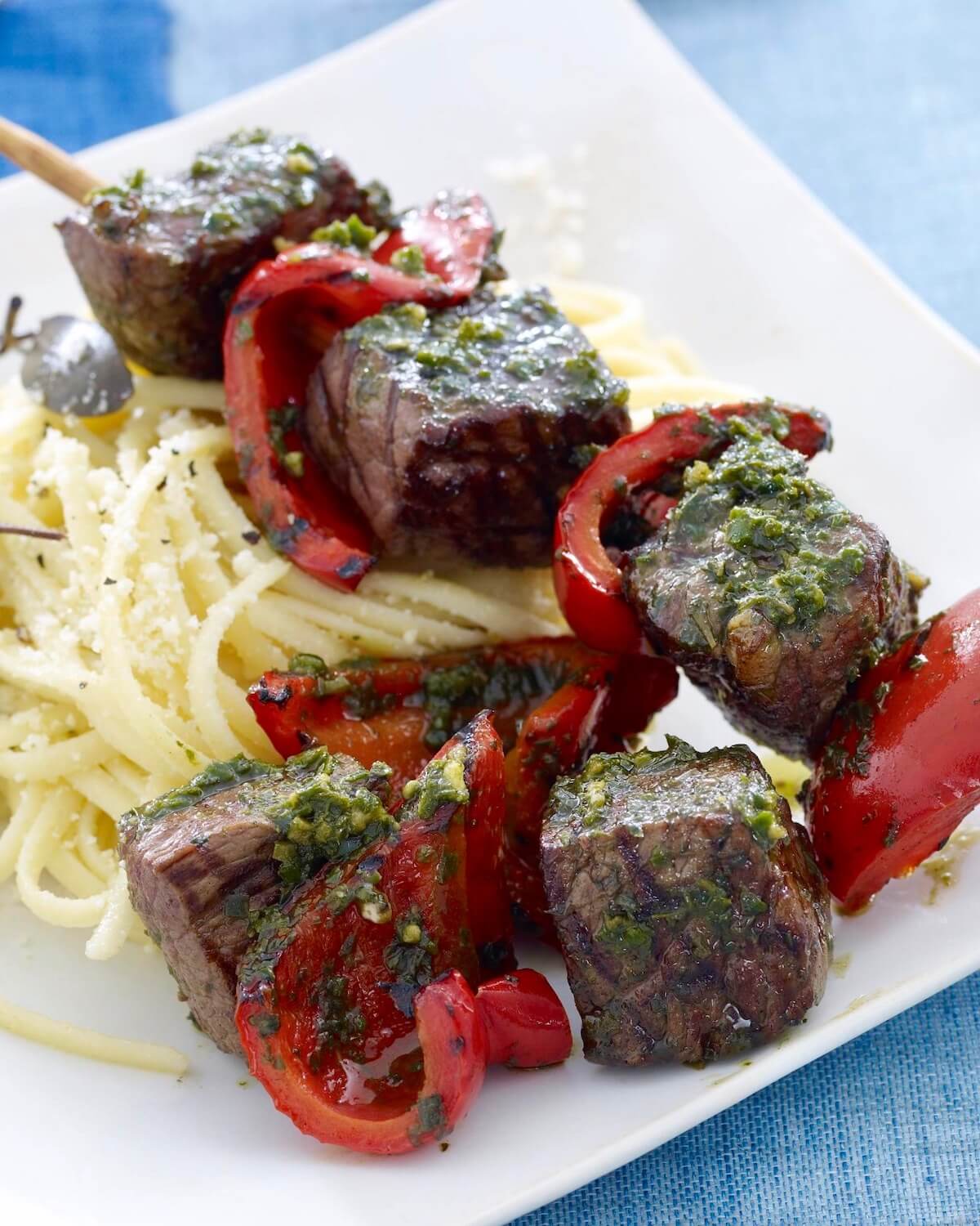 grilled beef kabobs with peppers and pasta on white plate