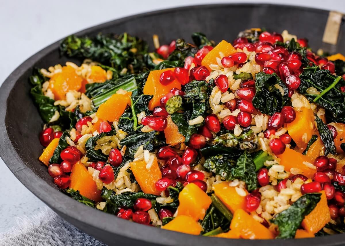 Close up of kale and squash salad with brown rice and pomegranates in a slate bowl.