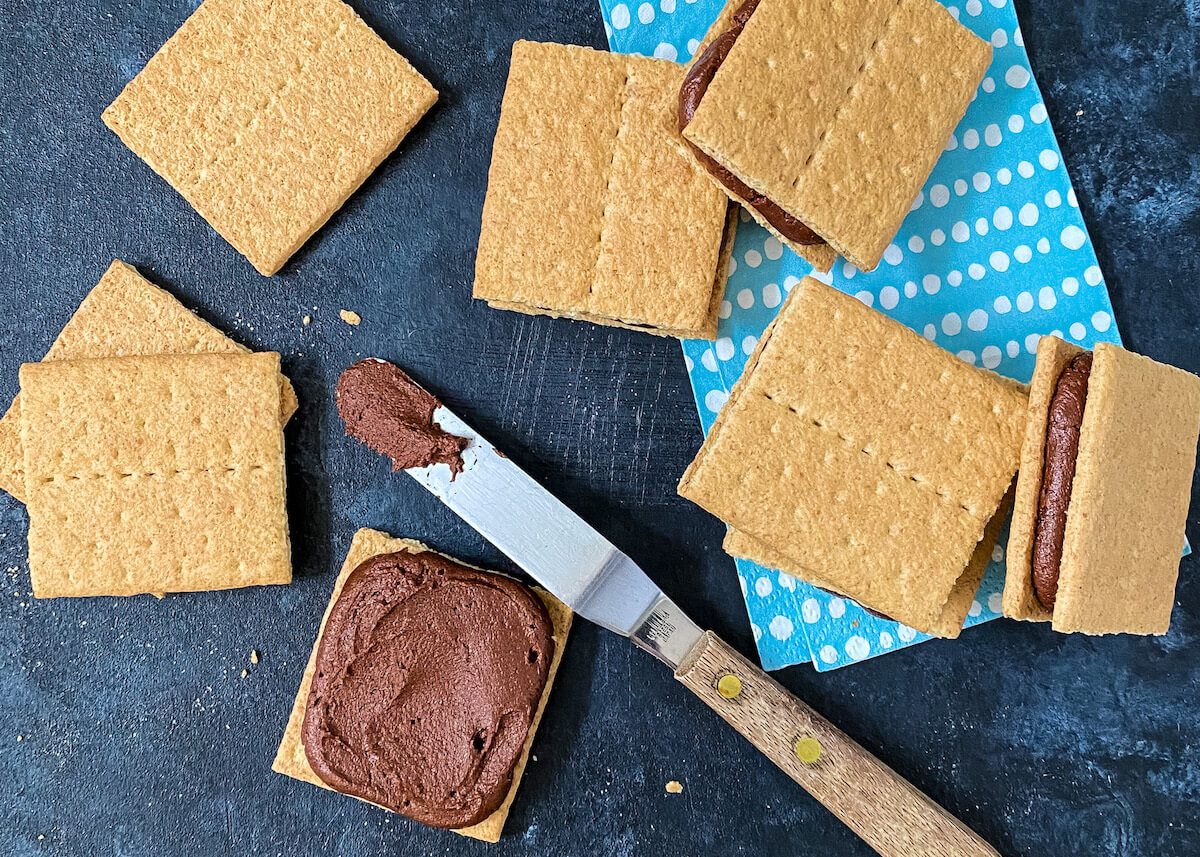spreading chocolate frosting on graham cracker cookies
