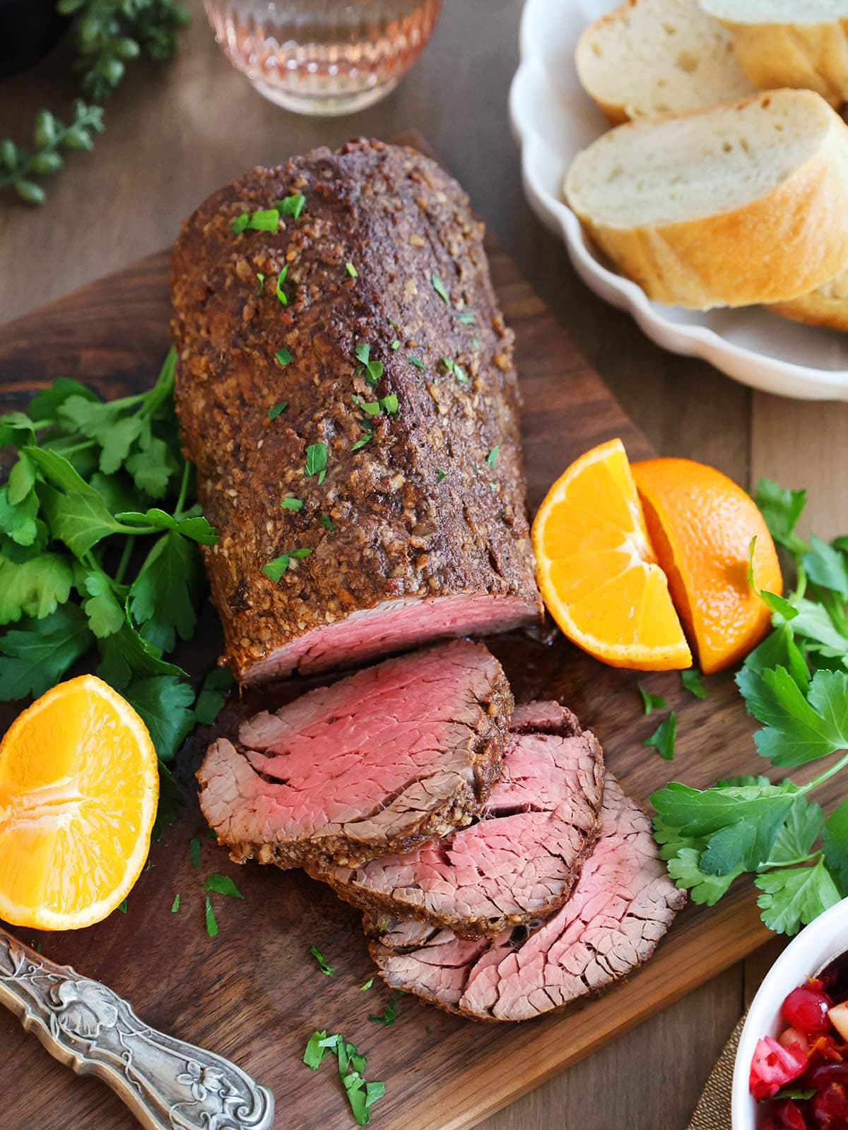 Top view of a beef tenderloin roast on a cutting board next to oranges and parsley.