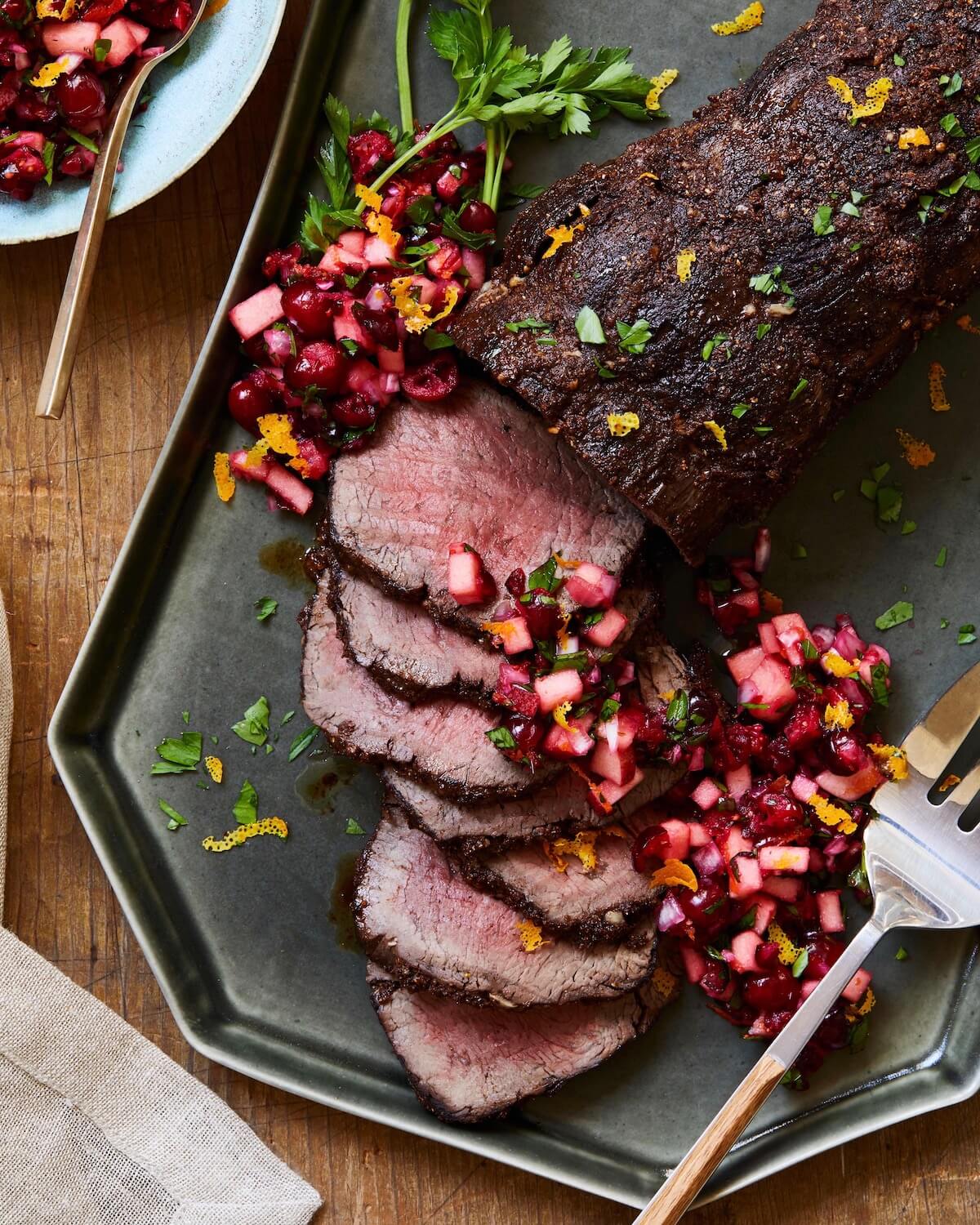 beef roast on platter with herbs and cranberry relish