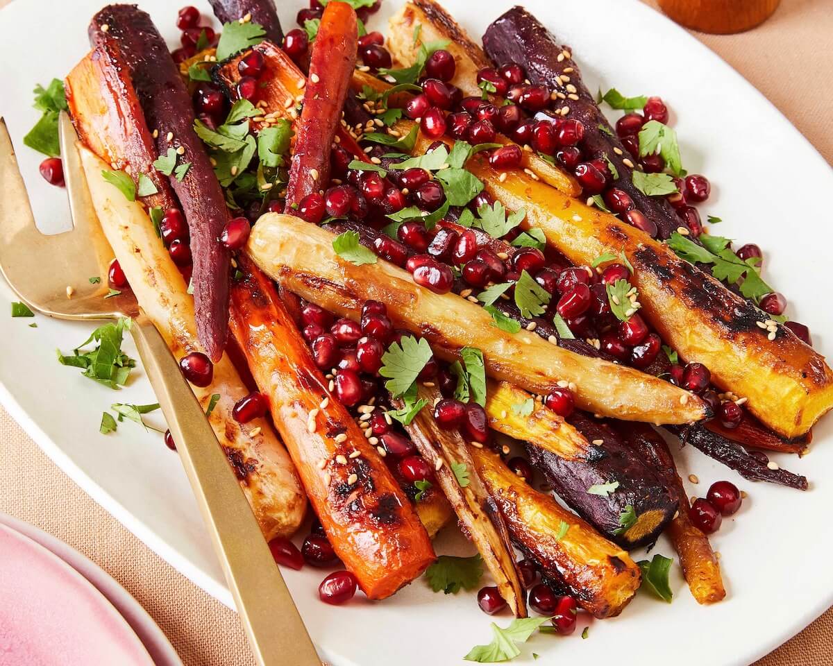 tricolor carrots on a white platter with pomegranates