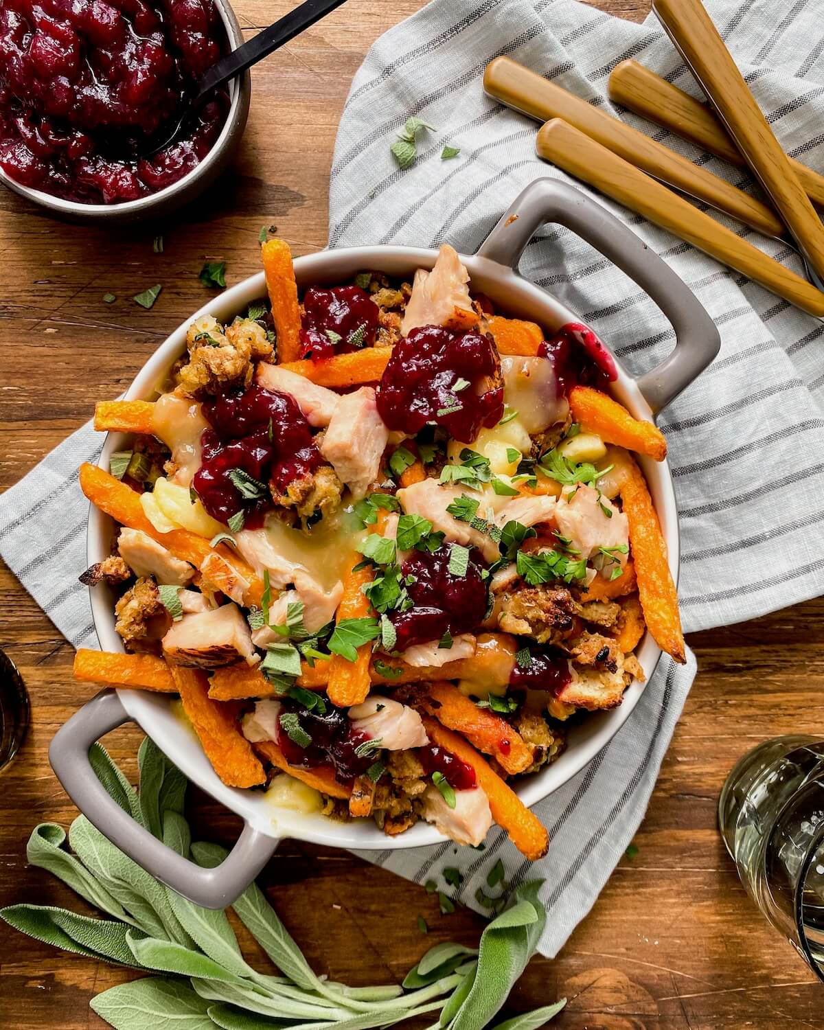 thanksgiving leftovers poutine in a baking dish with sage and cranberry sauce