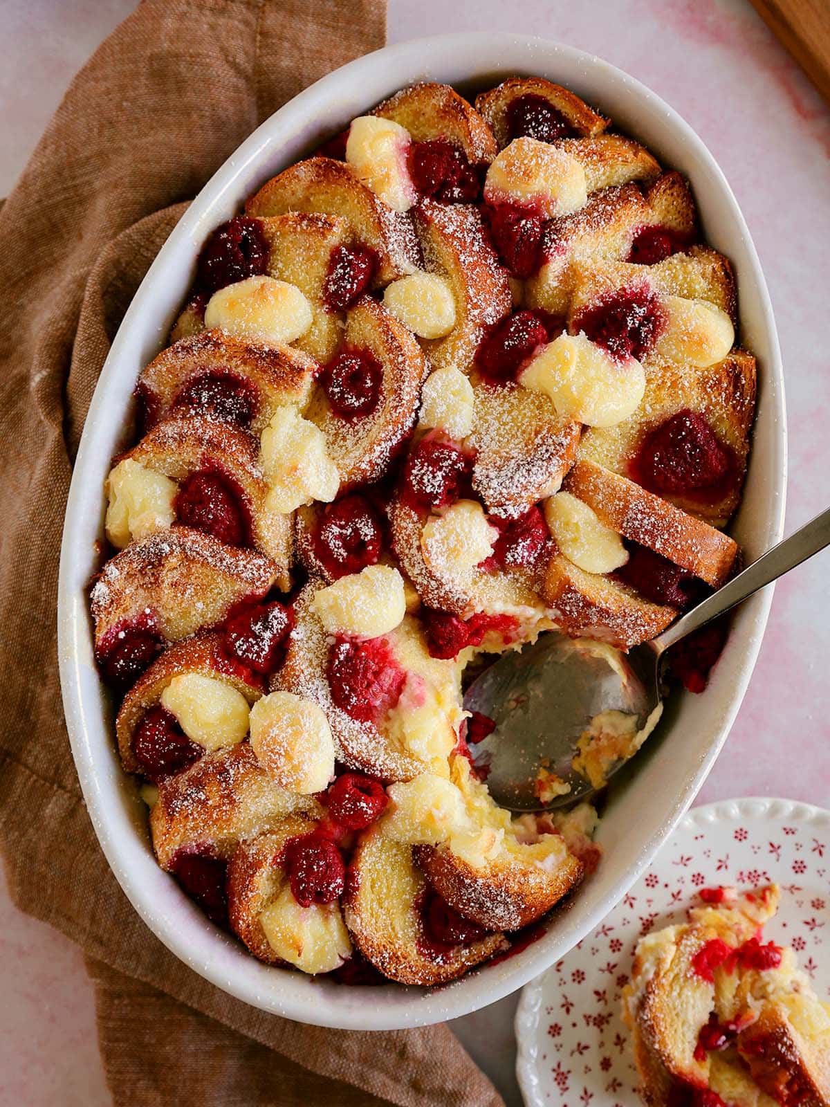 Raspberry bread pudding with a serving spoon inserted into the pan.