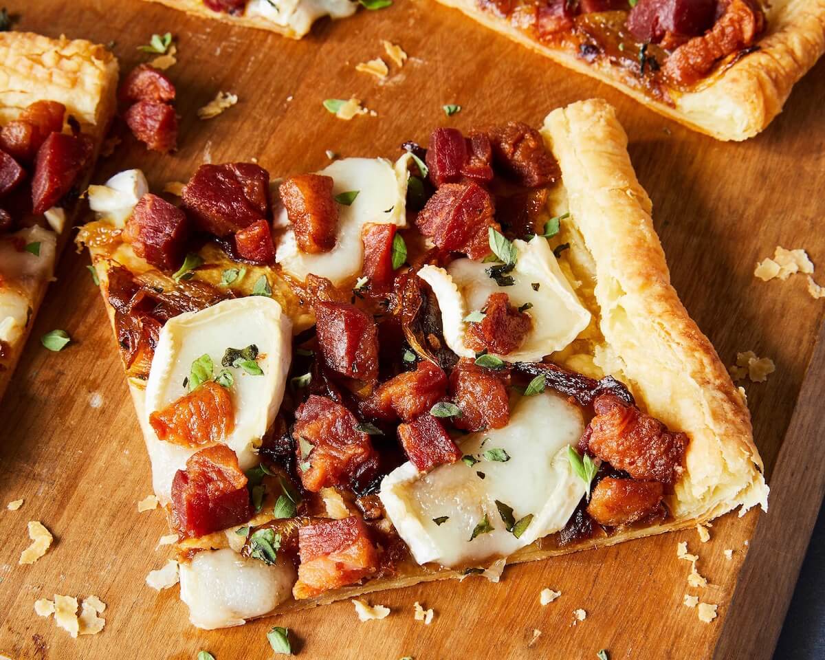 Close up of a slice of puff pastry caramelized onion tart with Brie and pancetta. 