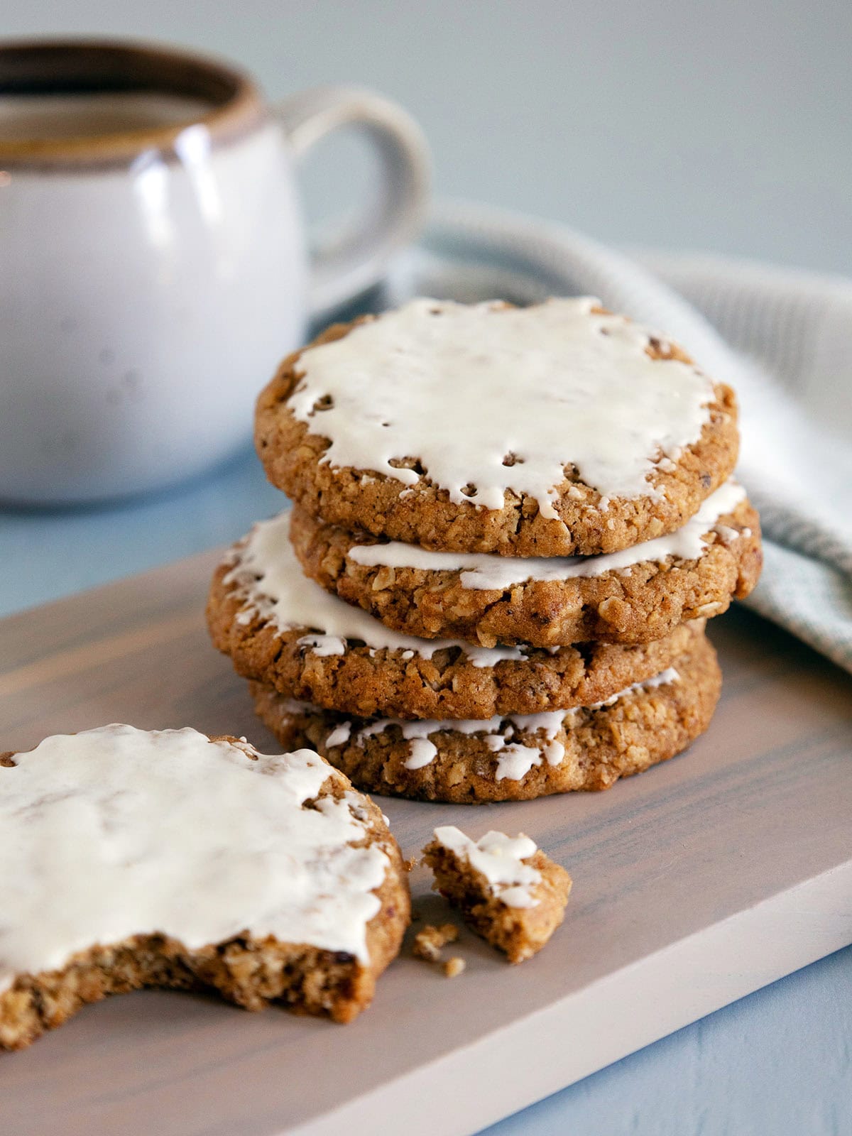 A stack of 3 iced oatmeal cookies with a broken cookie nearby.