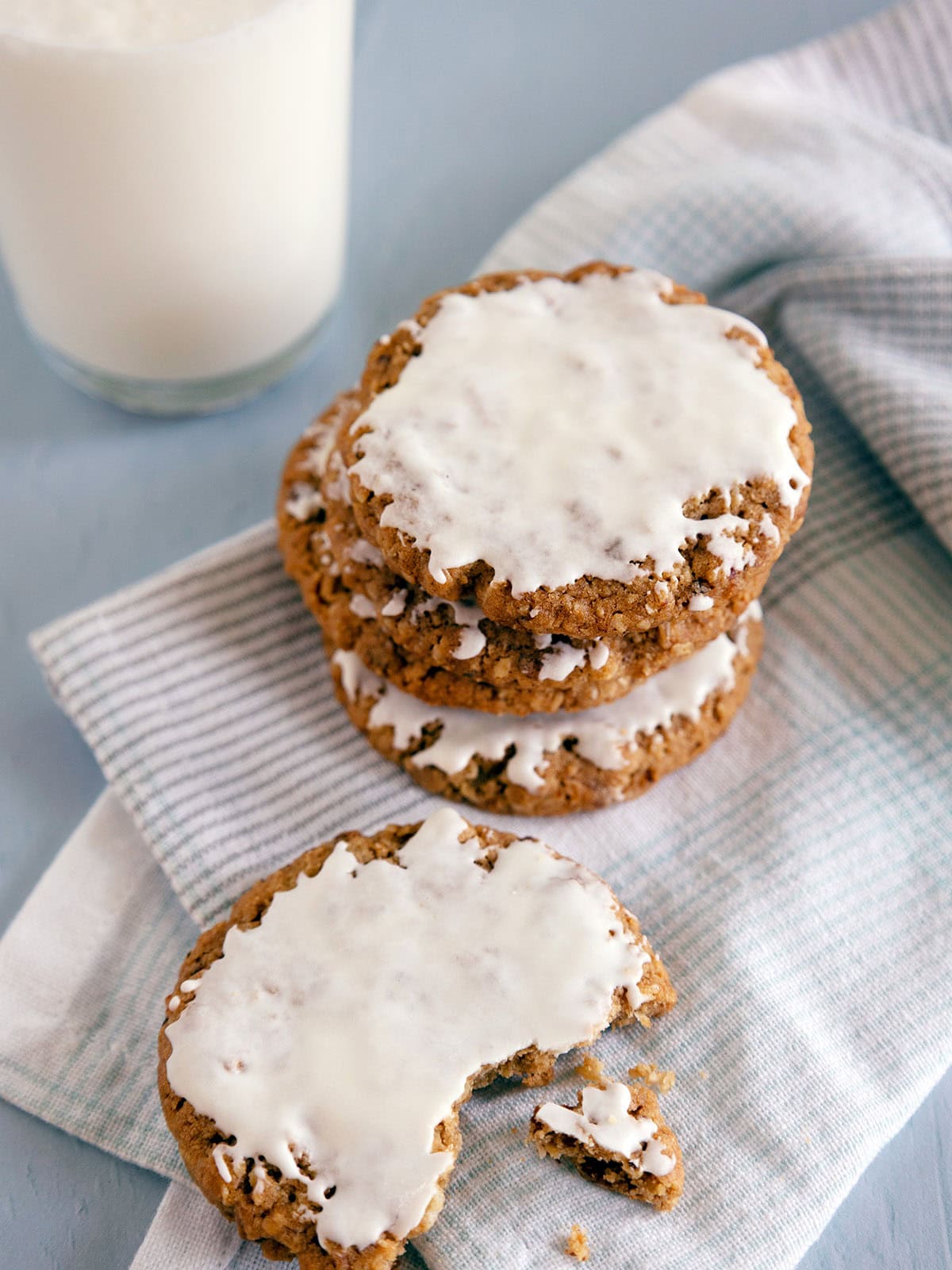 A stack of 3 iced oatmeal cookies on a napkin with another broken cookie in the foreground.