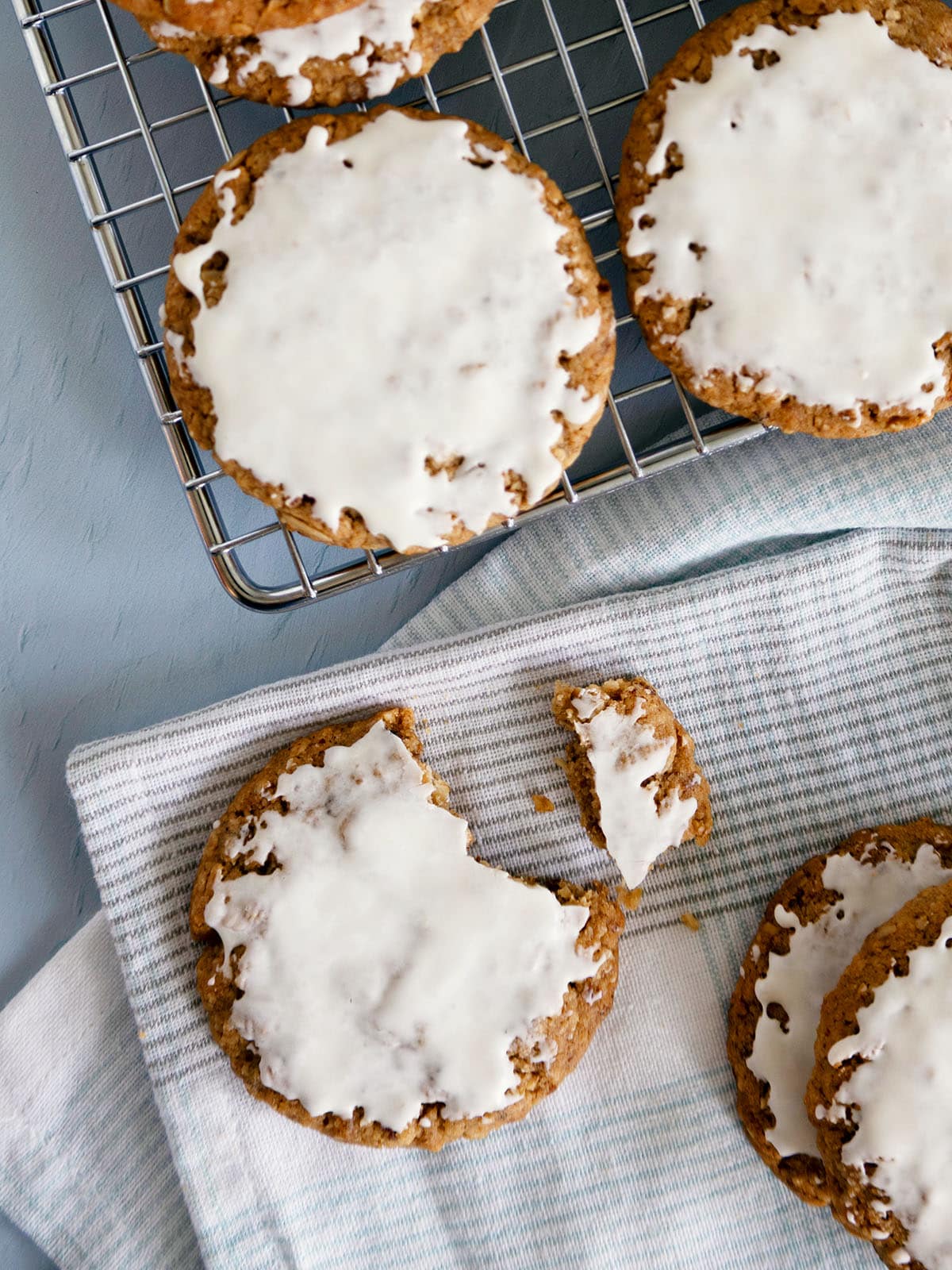 Iced oatmeal cookies on a wire rack with more cookies on a white napkin.