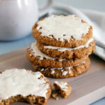 A stack of 3 iced oatmeal cookies with a broken cookie nearby.