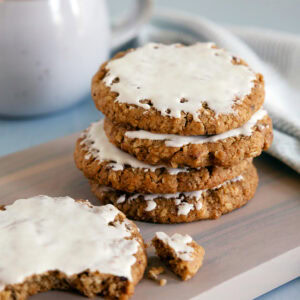 A stack of 3 iced oatmeal cookies with a broken cookie nearby.