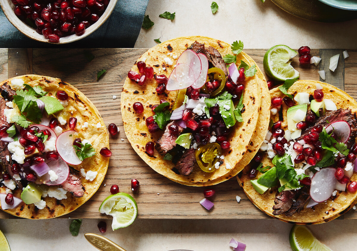 overhead view of three tacos with steak and pomegranates