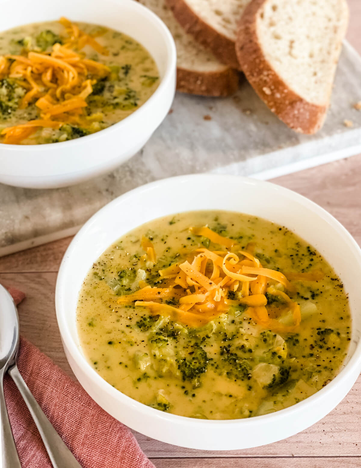 two bowls of broccoli cheddar soup with bits of broccoli showing