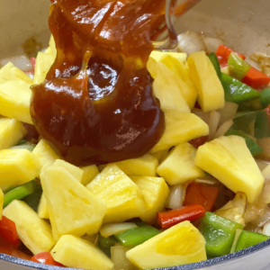 adding sauce and pineapple to sweet and sour chicken