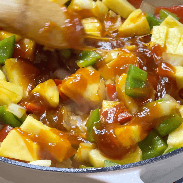 Wooden spoon stirring together sweet and sour chicken. 