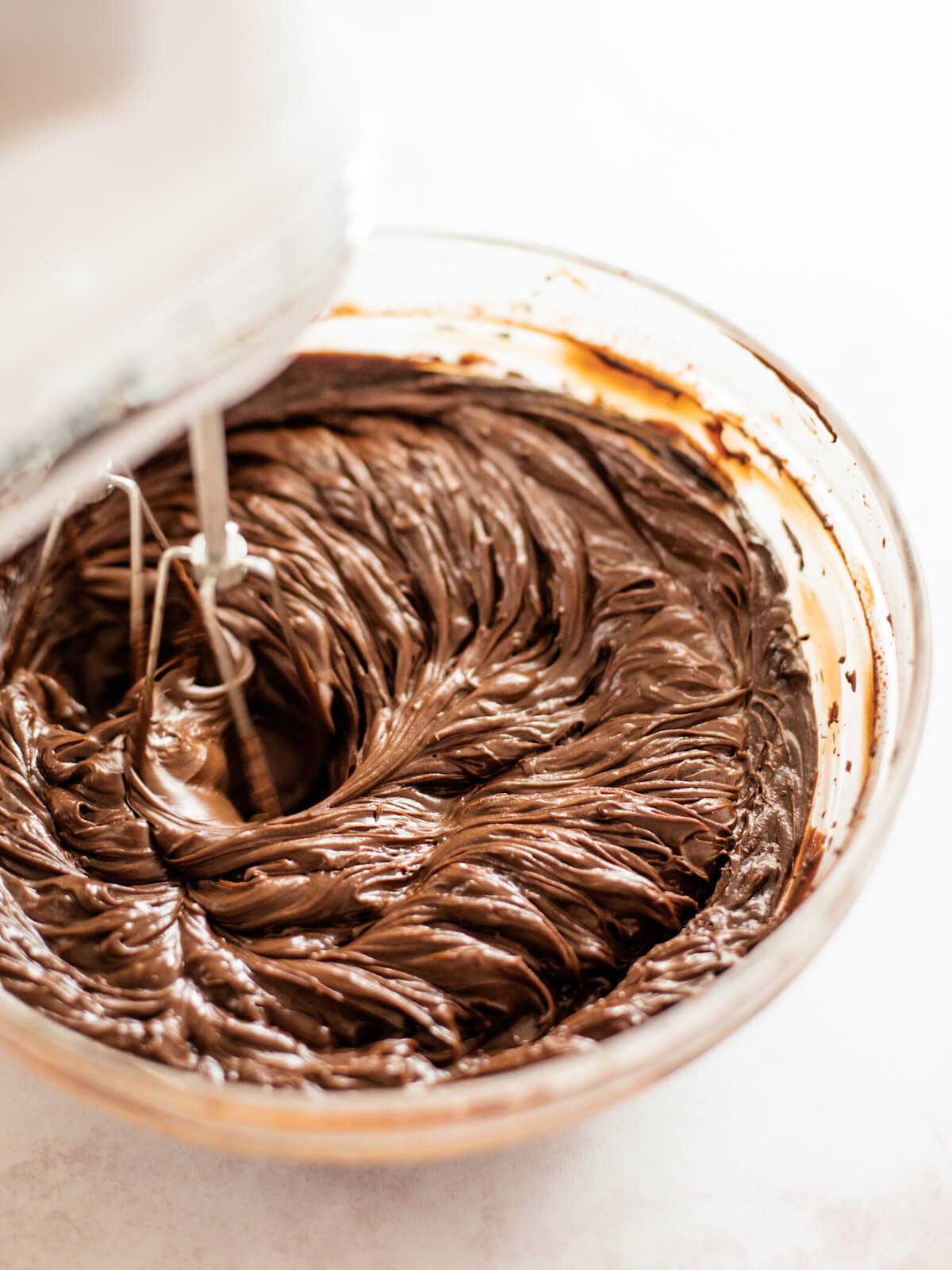 mixing chocolate ganache frosting in glass bowl
