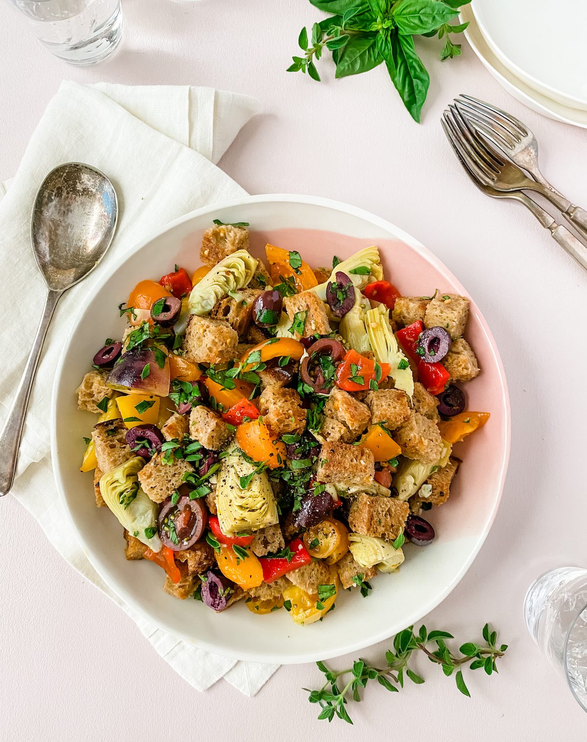 panzanella bread salad with artichokes in a pink bowl with herbs