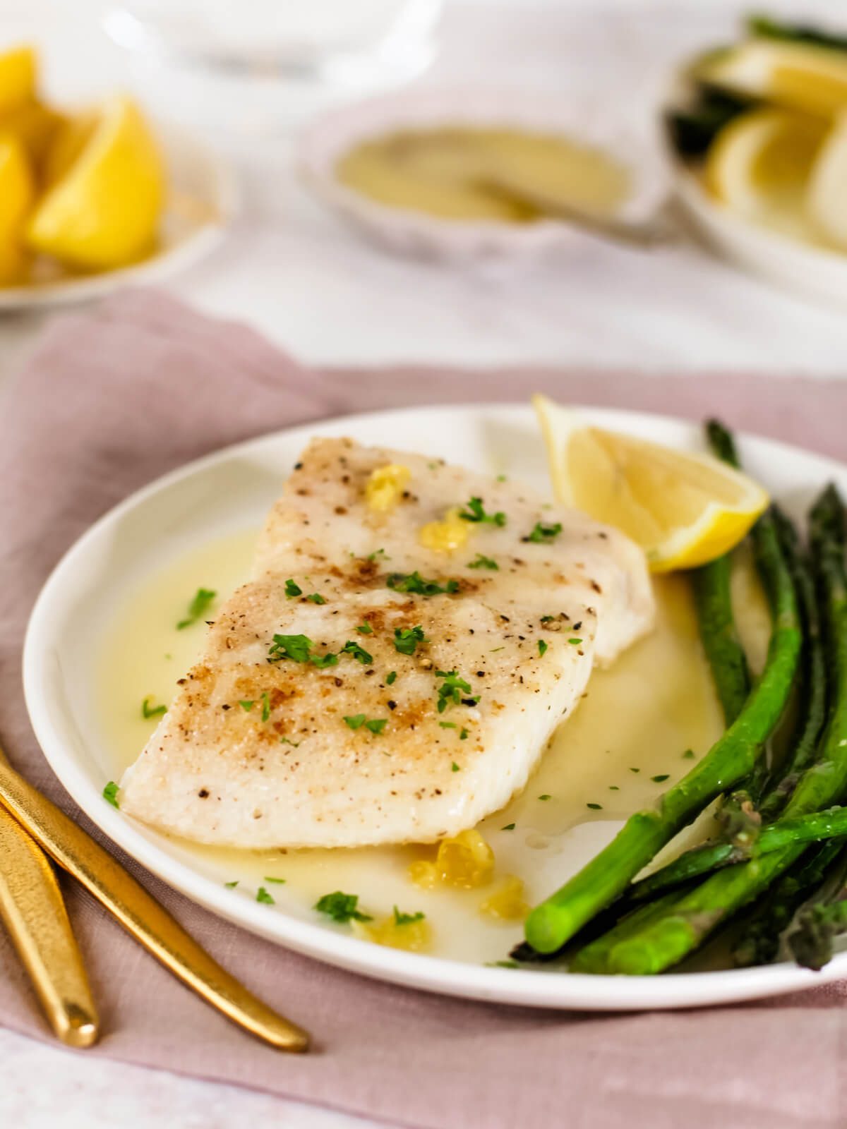 cooked fish with parsley and lemon sauce on a plate with asparagus