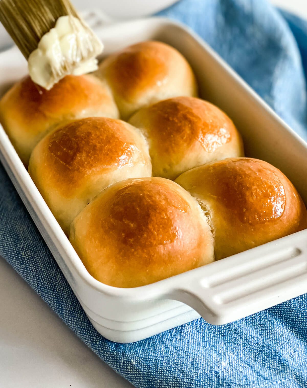classic dinner rolls in a baking dish being brushed with butter