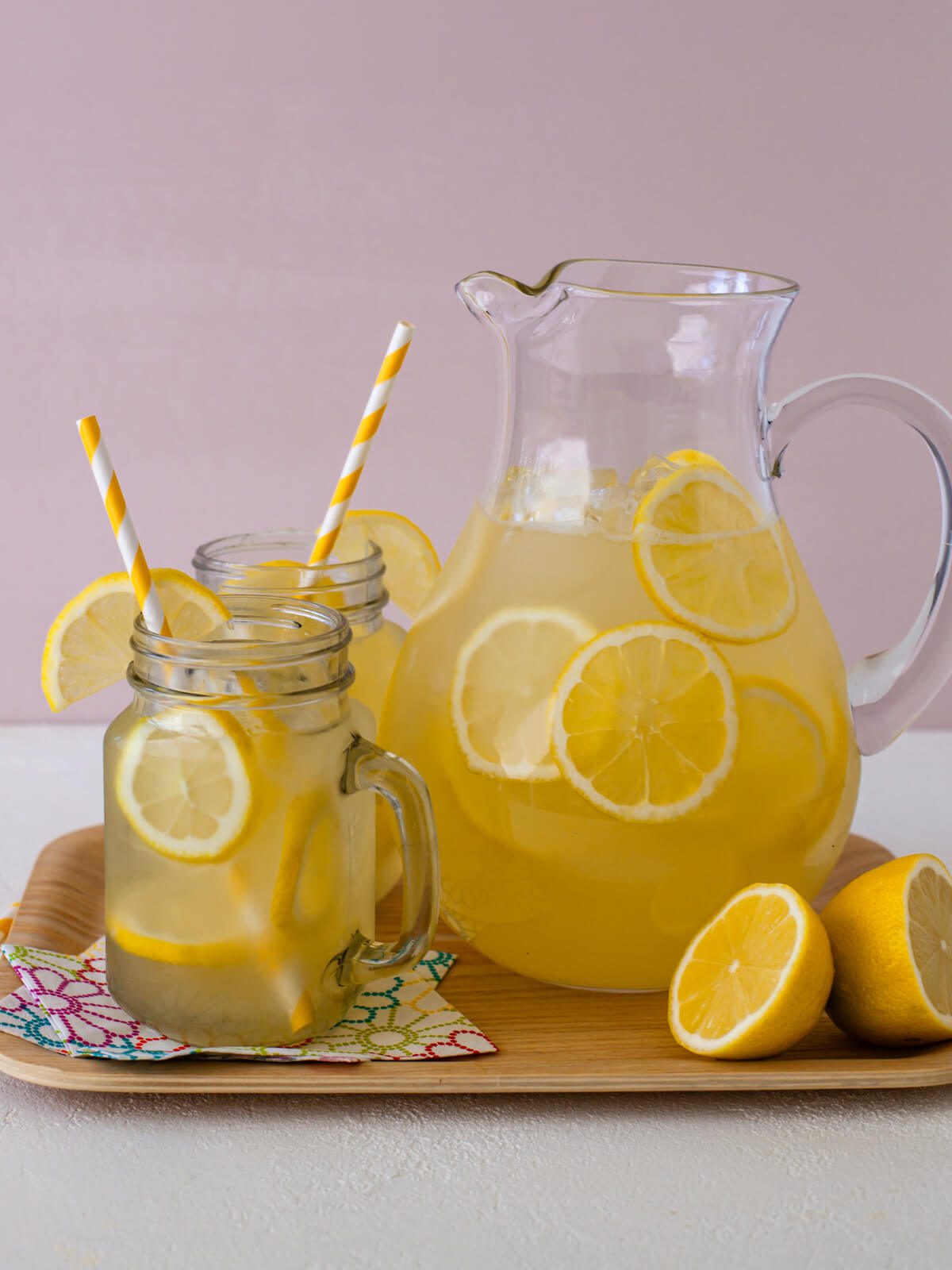 clear mugs of lemonade with straws and lemon slices and a pitcher of homemade lemonade