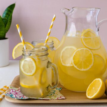 homemade lemonade in clear mug with pitcher of lemonade and lemon slices