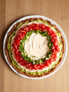 scallions and tomatoes being layered on 7 layer dip.