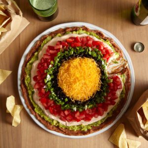 7 layer dip on a table with corn chips and beer.