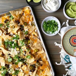 Sheet pan nachos on silver tray with cilantro, guacamole, sour cream and jalapenos.