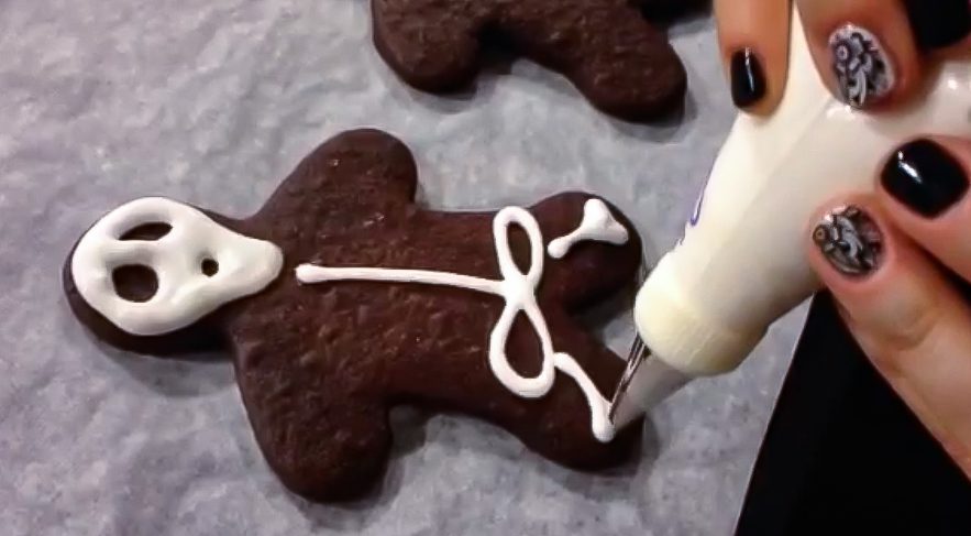 piping icing bones on a chocolate skeleton cookie with a piping bag and #2 small tip.