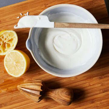 lemon royal icing in a bowl with a spatula and cut lemons on cutting board