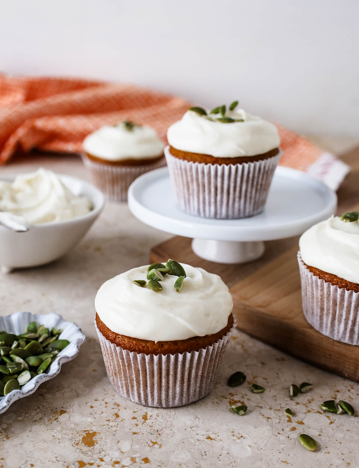 Several frosted pumpkin cupcakes in white papers on a table with a cutting board.