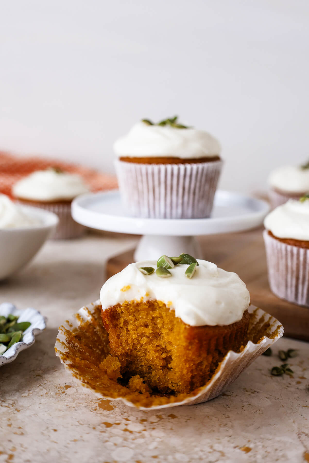 Pumpkin cupcake surrounded by other cupcakes on a stone table, with one bite taken out.