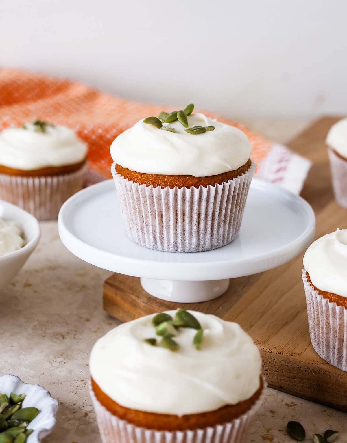Several pumpkin cupcakes on a table with one on a mini white pedestal.