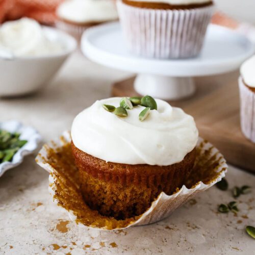 Just-opened pumpkin cupcake with muffin wrapper still on it, sitting on a stone surface with other cupcakes around.
