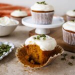 Pumpkin cupcake in opened muffin paper with a bite taken out and crumbs at the base.