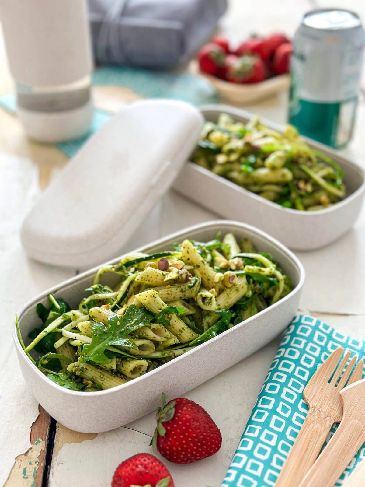 picnic meal in to go containers. pesto pasta with arugula, strawberries and soda.