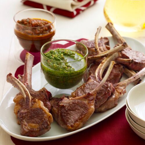 lamb chops on a platter with a dish of green herb sauce.