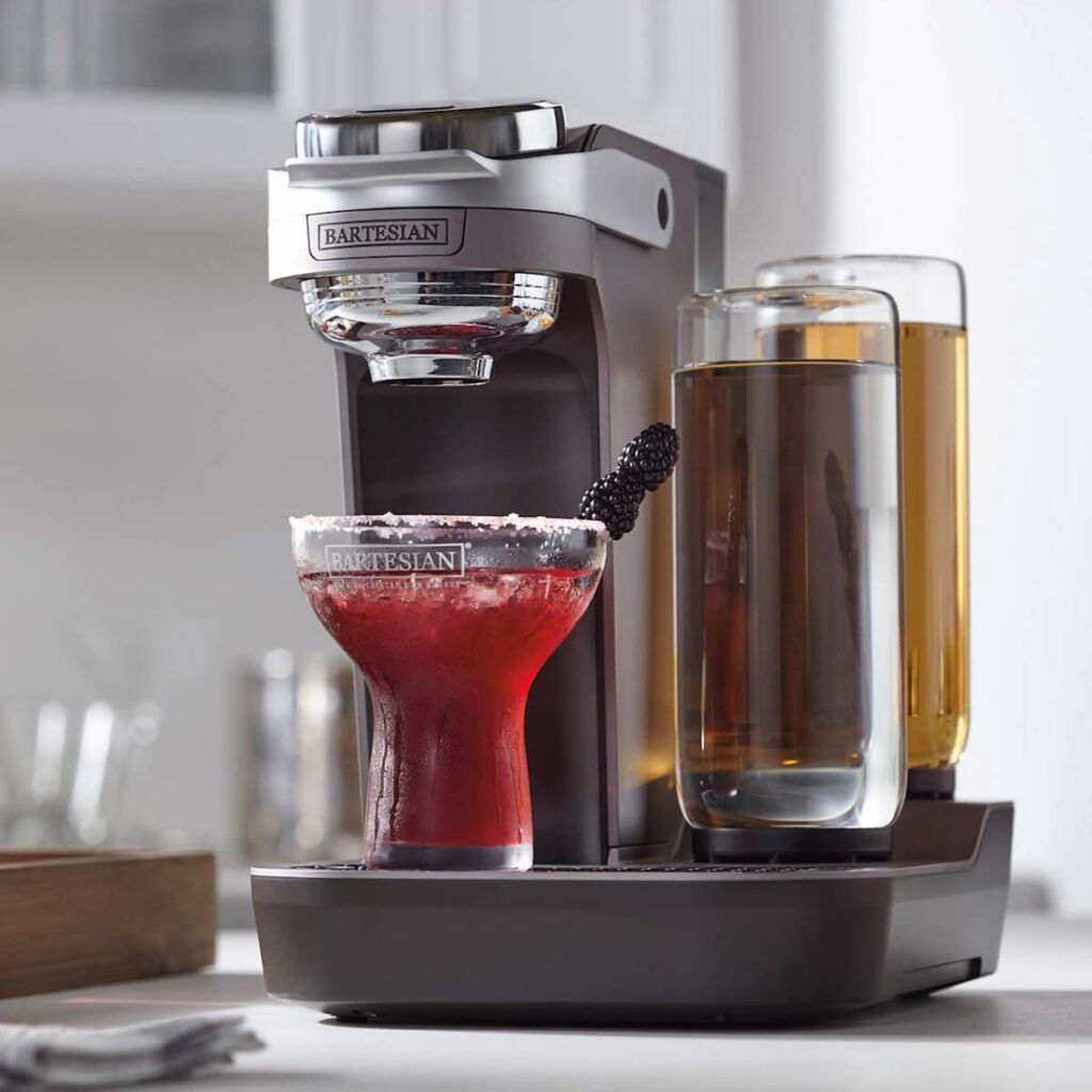 Black Bartesian duet cocktail maker machine set in a white kitchen, dispensing a berry-flavored cocktail into a glass.